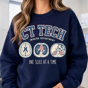 May include: A navy blue crewneck sweatshirt featuring the text CT TECH IMAGING DEPARTMENT and ONE SLICE AT A TIME in white and red. The graphic includes three circular medical cross-section illustrations of a brain, lungs, and abdomen.
