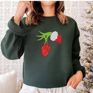 May include: A dark green sweatshirt with a graphic of a green hand wearing a Santa hat holding a red heart.
