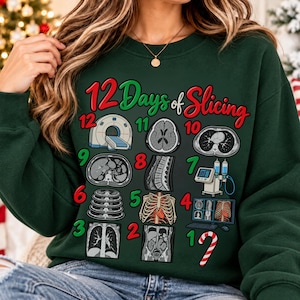 May include: A dark green crewneck sweatshirt featuring the text 12 Days of Slicing in red and green. The graphic includes twelve medical imaging illustrations, such as a CT scanner, cross-sectional body scans, and a candy cane, numbered 1 to 12.