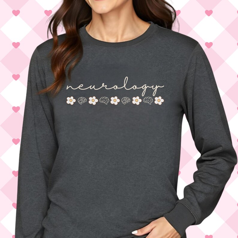 Puede incluir: Camiseta de manga larga gris oscuro con la palabra "neurology" en cursiva. Debajo, seis ilustraciones de cerebros se alternan con flores blancas con centros beige. La camiseta tiene cuello redondo y mangas largas.