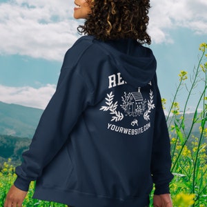 May include: A navy blue zip-up hoodie with a white graphic on the back. The graphic features a house with a wreath, keys, and the text "YOURWEBSITE.COM".