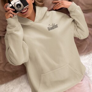 May include: A light beige hoodie with a large pocket on the front. The hoodie has the text "Cindy Realtor" printed on the front in black.
