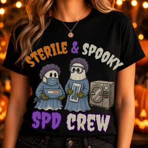 May include: A black t-shirt featuring a graphic of two ghosts dressed in blue surgical scrubs, caps, and masks. One ghost holds a tray, the other holds surgical tools next to an autoclave. Text reads: STERILE & SPOOKY SPD CREW.