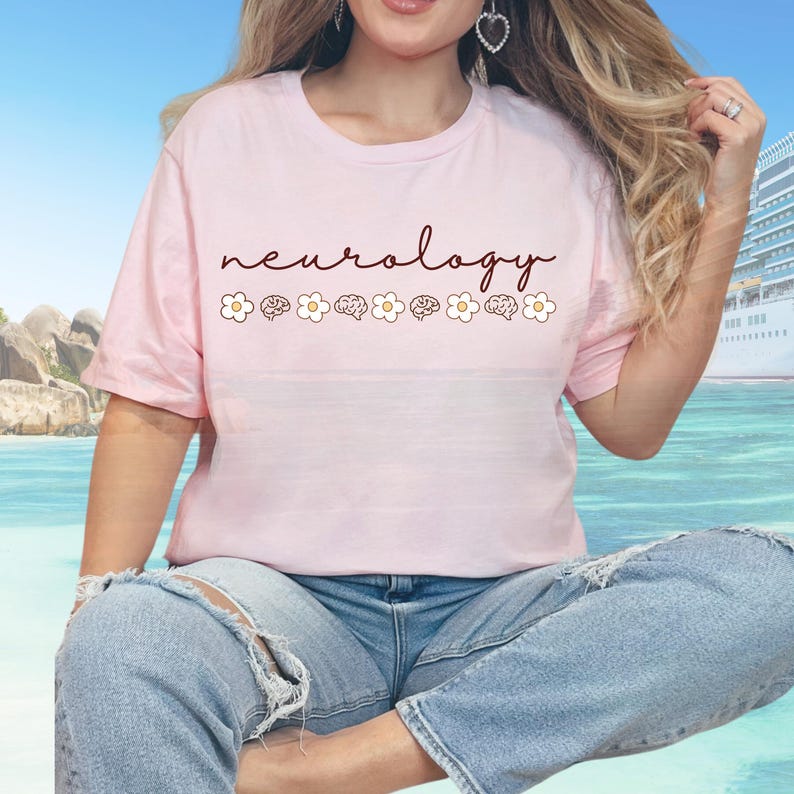 Puede incluir: Camiseta rosa claro con la palabra "neurology" en cursiva. Debajo, gr&aacute;ficos alternos de margaritas y cerebros. La camiseta es de un material suave y es adecuada para el uso diario.