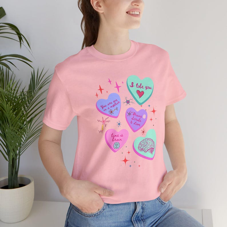 Puede incluir: Camiseta rosa con gr&aacute;ficos en forma de coraz&oacute;n en varios colores, incluyendo azul, verde y rosa. Los corazones presentan texto e ilustraciones relacionadas con el cerebro, con frases como "I love you" y "Time is brain".