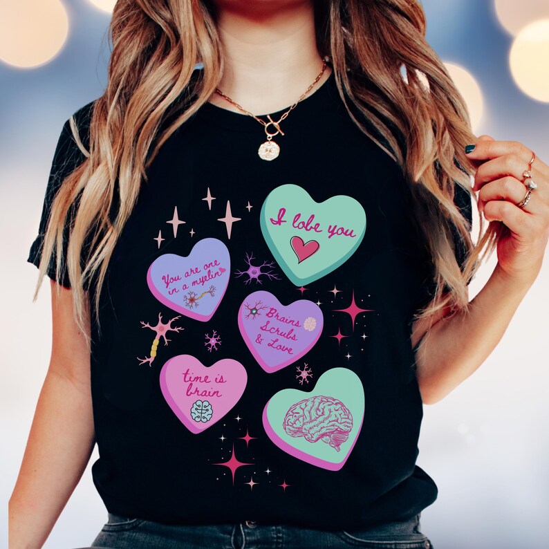 May include: Black t-shirt featuring five heart-shaped designs with science-themed text and illustrations. The hearts are various colors, including teal, purple, and pink, with phrases like "I lobe you" and "Brains Scrubs & Love."