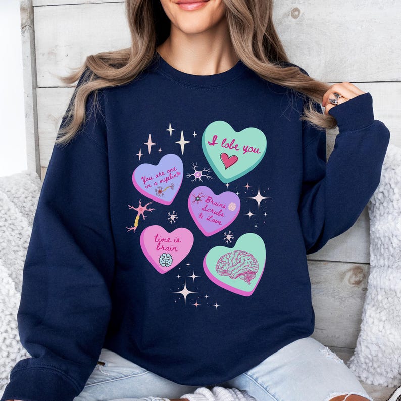 May include: Navy blue sweatshirt with heart-shaped graphics and text. The hearts feature phrases like "I lobe you," "You are one in a myelin," and "Time is brain." The design includes brain illustrations and star accents.
