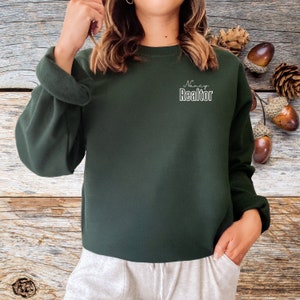 May include: A dark green sweatshirt with the text "Nancy Realtor" in white lettering on the front.