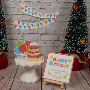 May include: A birthday cake with candles and colourful balloons on a white cake stand. A red card with the text "Happy Birthday" and "Hope your day is extra special!" is on a wooden easel.