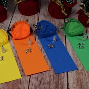 May include: Four miniature backpacks in different colors, yellow, orange, blue, and green, with a small water bottle and dumbbells next to each one.