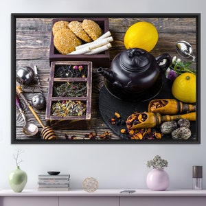 Könnte beinhalten: Eine schwarze Teekanne mit einem Holzgriff und -deckel, umgeben von losen Blatttee, Teebeuteln, Keksen, Zitronen und Honig. Die Szene spielt auf einem rustikalen Holztisch.