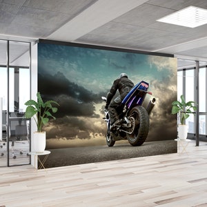 Può includere: Una moto blu e nera con un pilota in giacca di pelle nera e casco che guida su una strada con un cielo nuvoloso sullo sfondo.