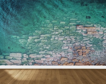 May include: A teal and brown textured wall with a white baseboard and a wood floor. The wall has a cracked and weathered look, resembling a stone wall.