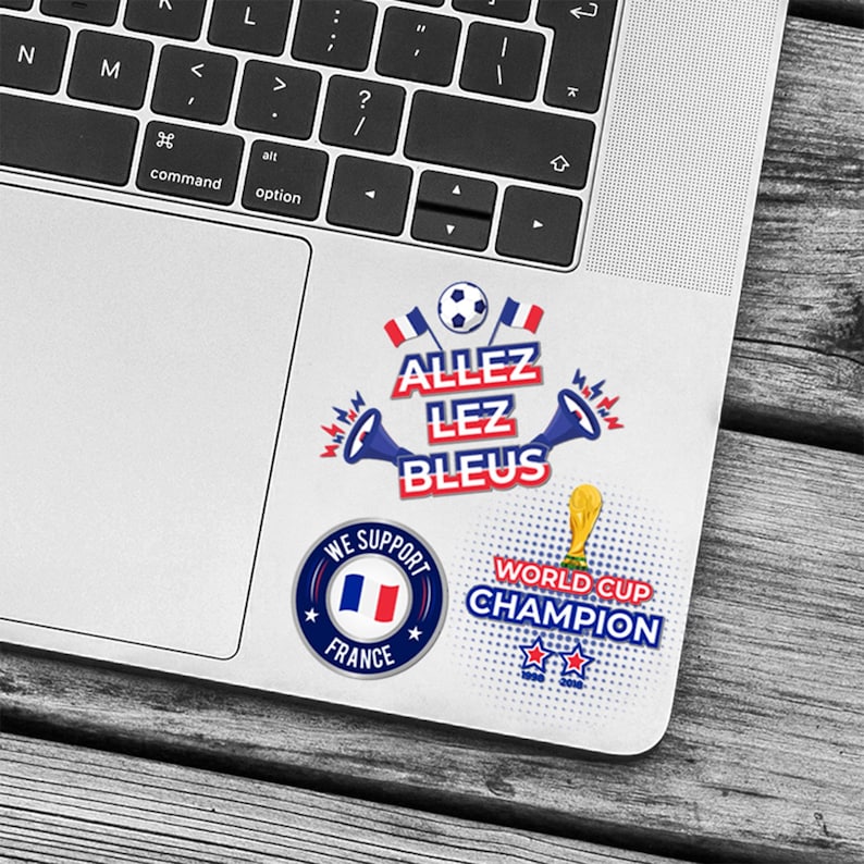 May include: A set of stickers featuring French football designs. The stickers include the text "ALLEZ LEZ BLEUS", a soccer ball, the French flag, and the words "WORLD CUP CHAMPION". The stickers are on a laptop.