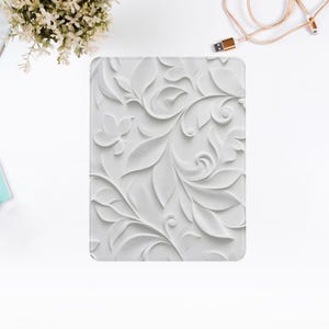 May include: White embossed floral design on a square tablet case. The design features intricate swirls and leaves.