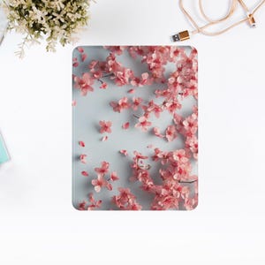 May include: A rectangular tablet case featuring a light blue background with a pattern of pink cherry blossom branches and scattered petals. The case has rounded corners and a glossy finish.