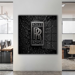 May include: A square wall art piece featuring the silver Rolls-Royce logo on a black background. The surface is covered in water droplets, creating a textured, wet appearance. The logo includes the text ROLLS above and ROYCE below the double R.