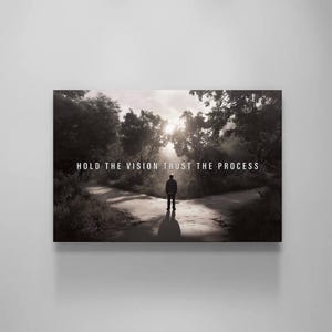 May include: Monochrome canvas print depicting a person at a forest crossroads, with the text "HOLD THE VISION TRUST THE PROCESS" in white. The image suggests reflection and choices, set in a natural environment.