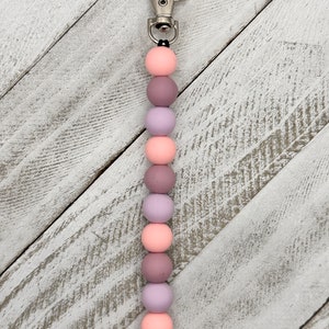 Puede incluir: Un llavero de cuentas rosa, morado y lavanda con un clip plateado.