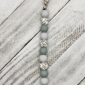May include: A gray and white beaded keychain with a silver clip. The beads have a floral pattern.