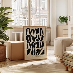 May include: A black and white abstract art print with the text "FORME NATURELLE.  Explorer la Nature et Ronger Avec le Vent."  The print is framed and hanging on a wall in a living room.