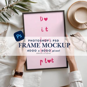 Könnte beinhalten: Ein schwarz gerahmter rosa Druck mit den Worten "Do it" und "plot" in rosa Schrift. Die Worte "FRAME MOCKUP" sind ebenfalls sichtbar. Ein Photoshop-Logo befindet sich in der Ecke. Der Rahmen wird von einer Person gehalten.