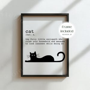 Könnte beinhalten: Schwarz gerahmter Kunstdruck mit einer schwarzen Katzenillustration und der Definition von "Katze". Der Text beschreibt das Verhalten einer Katze. Rahmenmaße: 30 x 40 cm.