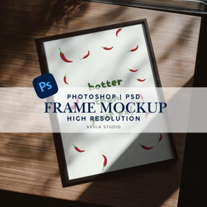 Könnte beinhalten: Ein gerahmter Druck mit weißem Hintergrund und roten Chili-Pfeffer-Illustrationen. Das Wort "hotter" ist in grüner Schrift geschrieben. Der Rahmen ist dunkelbraun. Der Text "FRAME MOCKUP" wird in großen, fetten Buchstaben angezeigt.
