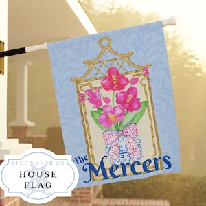 May include: A blue and white house flag with a pink orchid floral design in a bamboo frame. The text "The Mercers" is printed in blue on the flag.