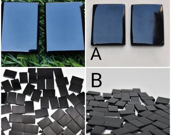 May include: A collection of black rectangular tiles with a smooth, glossy finish. The image displays two larger tiles side-by-side and two separate groups of numerous smaller, uniform rectangular tiles arranged in a scattered, overlapping pattern.