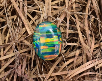 May include: An oval-shaped doublet gemstone featuring a dark base with vibrant, multi-colored flashes of green, blue, orange, and yellow. The surface is polished and smooth, displaying a mosaic-like pattern of iridescent color segments.