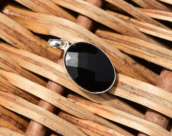 May include: An oval-shaped black gemstone pendant set in a polished silver metal frame. The gemstone features a faceted surface that reflects light, and the pendant includes a small silver bail at the top for attachment to a chain or necklace.