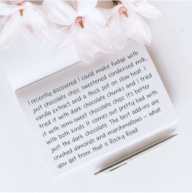 May include: A handwritten note on white paper with a silver pen resting on top. The note describes a recipe for fudge with chocolate chips, condensed milk, vanilla extract, and chocolate chunks. The note mentions that the best add-ins are crushed almonds and marshmallows.