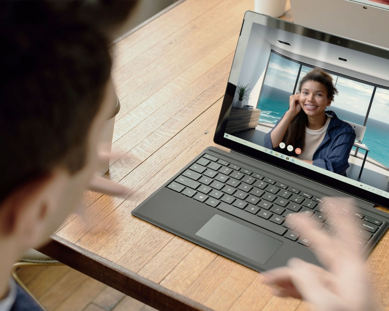 May include: A person is on a video call on a black laptop with a keyboard and trackpad. The person on the screen is smiling and has long dark hair. The laptop is on a wooden table.
