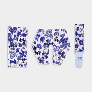 Op de afbeelding: Een set van drie stoffen accessoires met een blauw-wit bloemenpatroon. De set bevat een rechthoekige band met drie metalen drukknopen, een U-vormig stuk met twee drukknopen en een band met een enkele metalen drukknoop en een lichtblauwe clip.