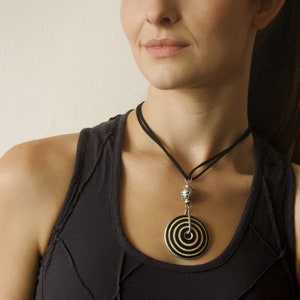 May include: A black and white circular pendant necklace with a silver bead and a black cord. The necklace is worn by a person with a black tank top.