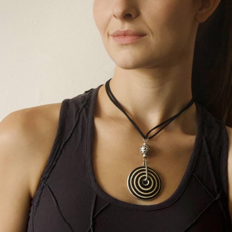 May include: A black and white circular pendant necklace with a silver bead and a black cord. The necklace is worn by a person with a black tank top.