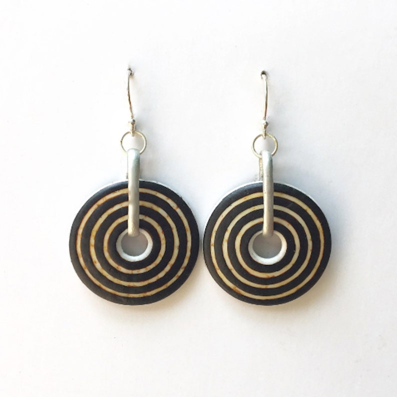 May include: A pair of silver hoop earrings with black and white concentric circles. The circles have a wood-like texture.