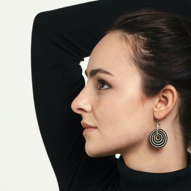 May include: A woman wearing a black turtleneck sweater with a pair of black and white circle earrings.