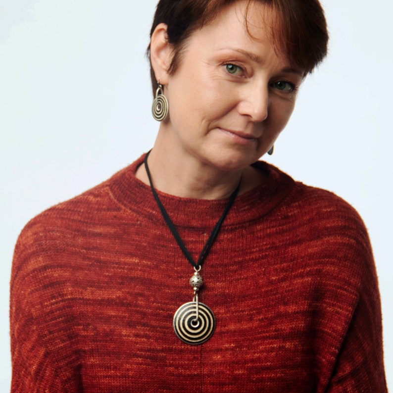 May include: A woman wearing a red sweater with a black and white circular pendant necklace and matching earrings.
