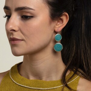May include: A pair of silver dangle earrings with turquoise blue circular designs. The earrings have two circles on each dangle, with the top circle being slightly smaller than the bottom circle.