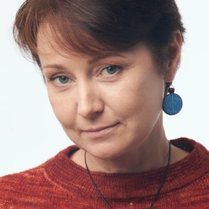 May include: A woman with short brown hair wearing a red sweater and blue and white earrings.
