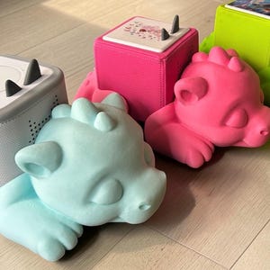Può includere: Una collezione di basi per altoparlanti e altoparlanti colorati a forma di drago. Gli altoparlanti sono in vari colori, tra cui grigio, rosa, verde e blu. Le basi sono progettate per contenere gli altoparlanti.