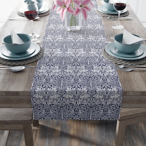 Könnte beinhalten: Ein dunkelblauer Tischläufer mit einem weißen Blumen- und Hasenmuster. Der Läufer liegt auf einem Holztisch mit Gedecken auf beiden Seiten.