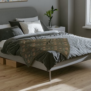 K&ouml;nnte beinhalten: Ein graues Bett mit einer gr&uuml;n-braunen, gemusterten Tagesdecke. Das Bett hat ein graues Kopfteil und ein wei&szlig;es Kissen mit einem karierten Muster.