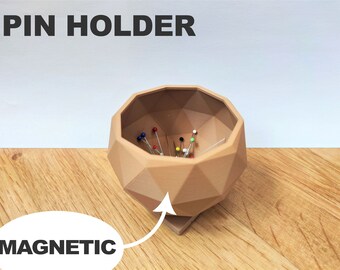 May include: A geometric, light brown pin holder with the word "PIN HOLDER" above it. The pin holder is filled with colorful pins. The word "MAGNETIC" is written below the pin holder.