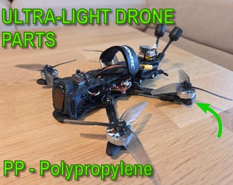 May include: A black ultra-light drone with four propellers, various electronic components, and the text "ULTRA-LIGHT DRONE PARTS" and "PP - Polypropylene" in green. The drone is on a wooden surface.