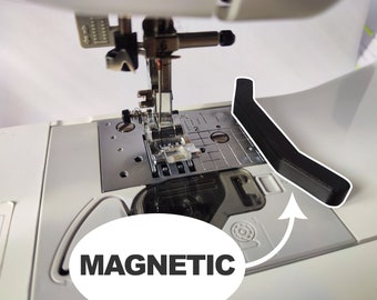 May include: A close-up of a sewing machine with a black magnetic attachment. The attachment is labeled "MAGNETIC" and is located on the right side of the machine.