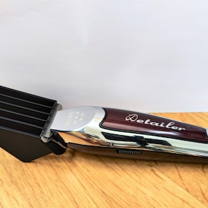 May include: A silver and burgundy electric hair clipper with a black comb attachment. The clipper has a silver detailer label on the side.