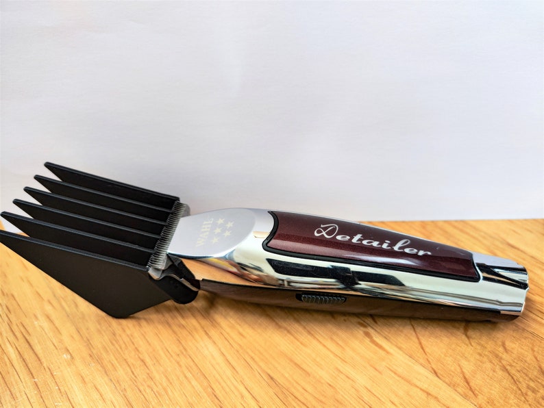 May include: A silver and burgundy electric hair clipper with a black comb attachment. The clipper has a silver detailer label on the side.